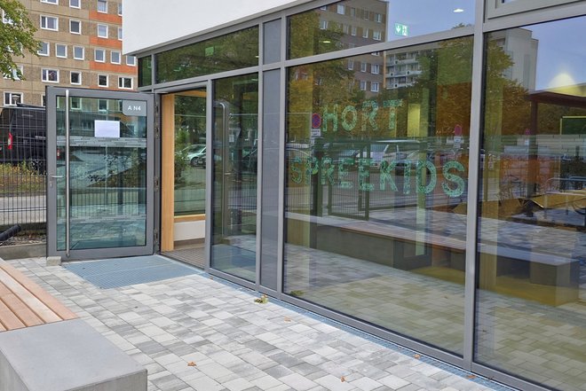 Eingangsbereich des modernen Gebäudes mit großen Glasfronten, auf denen die Schrift 'HORT SPEEKIDS' zu sehen ist