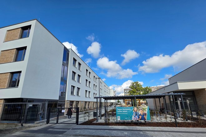 Hort Spreekids - Außenansicht Mehrstöckiges modernes Wohngebäude mit weißer Fassade und braunen Fensterrahmen bei blauem Himmel mit Wolken