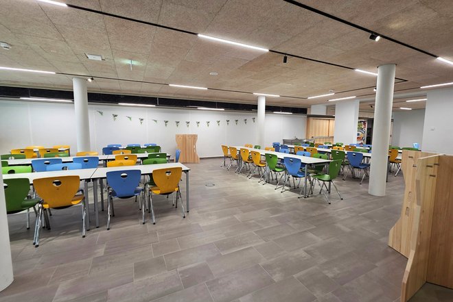 Großer heller Speisesaal mit mehreren Reihen Tischen und bunten Stühlen in Gelb, Blau und Grün