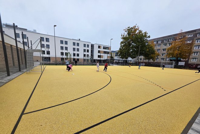 Hort Spreekids - Kinder spielen auf einem gelben Sportplatz mit schwarzen Linien in einem Wohngebiet