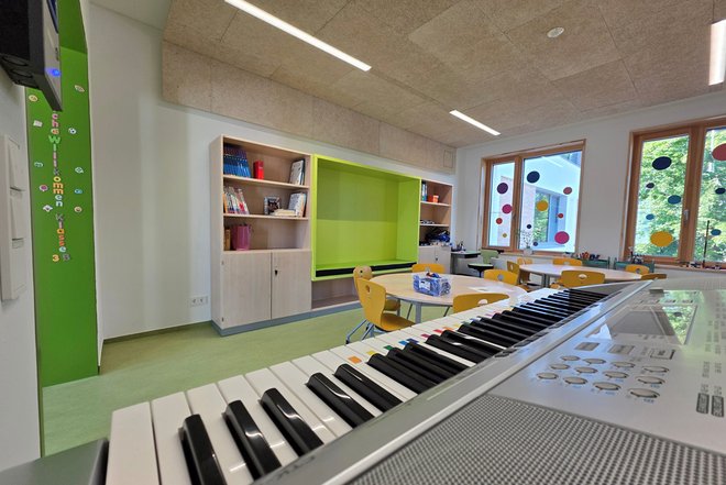 Musikraum mit Keyboard im Vordergrund, gelben Stühlen, Tischen und Regalen vor einer grünen Wand