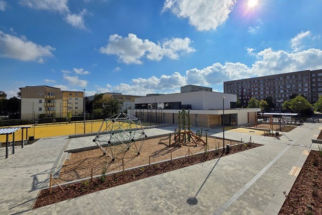 Spreekids - Moderner Spielplatz mit Klettergerüst und Schaukeln in einem urbanen Wohngebiet unter blauem Himmel mit Wolken